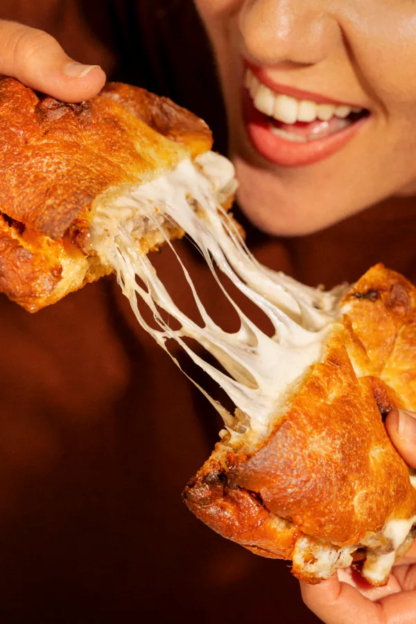 Smiling woman bisecting a salty bomba with stringy cheese inside