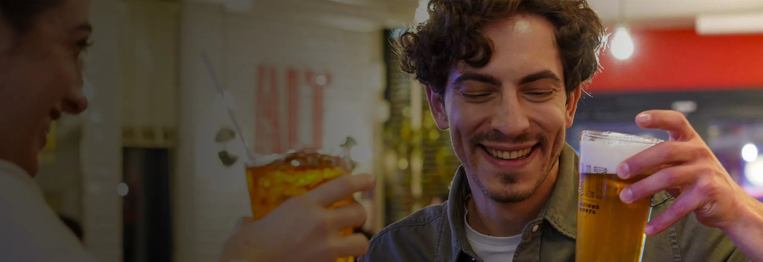 Giovane uomo con bicchiere di birra in mano che degusta un aperitivo in compagnia di amici - Young man with glass of beer in hand enjoying an aperitif with friends